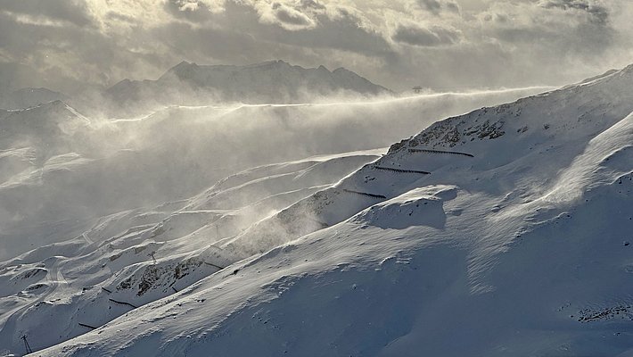 Schneebedeckte Berglandschaft mit wehenden Schneeverwehungen unter bewölktem Himmel
