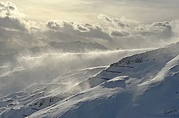 Schneebedeckte Berglandschaft mit wehenden Schneeverwehungen unter bewölktem Himmel