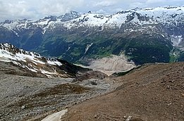 Berglandschaft mit schneebedeckten Gipfeln und einem felsigen, schneefreien Hang im Vordergrund
