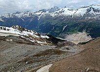 Berglandschaft mit schneebedeckten Gipfeln und einem felsigen, schneefreien Hang im Vordergrund