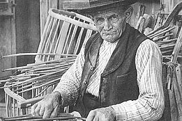 Historische schwarz-weiss Fotografie. Älterer Mann in traditioneller Kleidung und Hut fertigt Tragkörbel aus Holzstäben