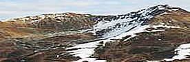 Berglandschaft mit schneebedeckten und schneefreien Flächen unter bewölktem Himmel