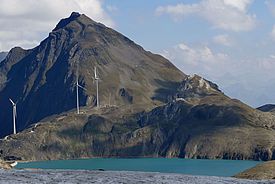 Windräder auf einem Bergkamm hinter einem schmelzenden Gletscher unter blauem Himmel mit Wolken