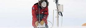 Forscher in rotem Parka arbeitet mit Messgerät auf verschneitem Eisfeld.