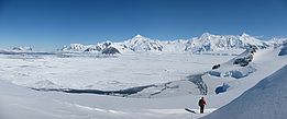 Person in roter Jacke wandert auf schneebedecktem Gelände mit Blick auf gefrorene Landschaft und schneebedeckte Berge in der Antarktis.
