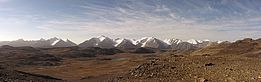 Weites Hochplateau in Kirgisistan mit brauner Tundra, kleinen Seen und schneebedeckten Bergen am Horizont