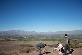 Drei Männer begutachten die Bodenverhältnisse auf einem trockenen Feld mit Blick auf ein Tal und Berge im Hintergrund