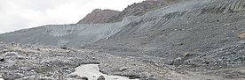 Schottriges Vorfeld des Findelengletschers in der Schweiz mit einem kleinen Bachlauf und Bergen im Hintergrund