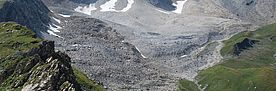 Blockgletscher oberhalb der Alp Flix. Der Blockgletscher selbst sieht aus wie eine Geröllhalde. Allerdings wird das Gestein durch die Vergletscherung so befestigt,  dass die Neigungswinkel viel steiler sind als bei lockerem, frei liegendem Geröll. Der grau-beige Blockgletscher ist links und rechts von grünen Hängen eingerahmt.